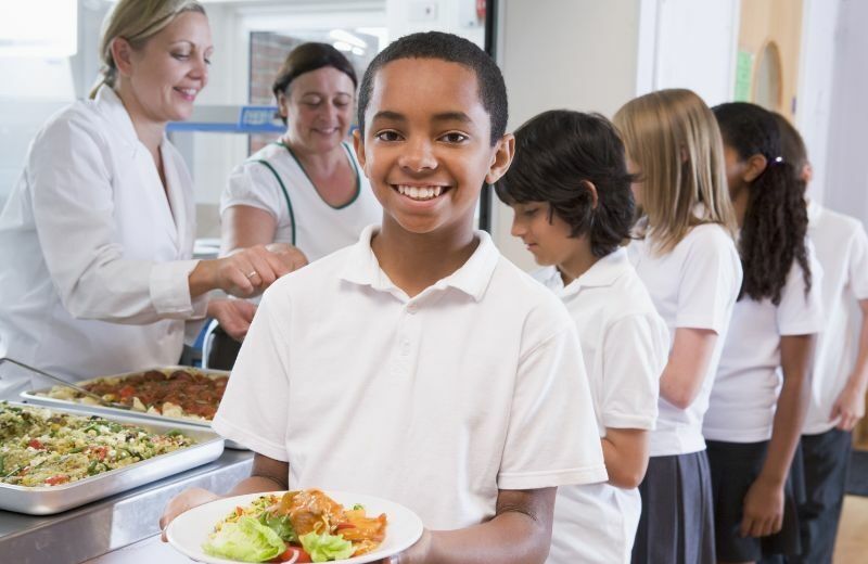 Queue in school canteen with children holding plates of food